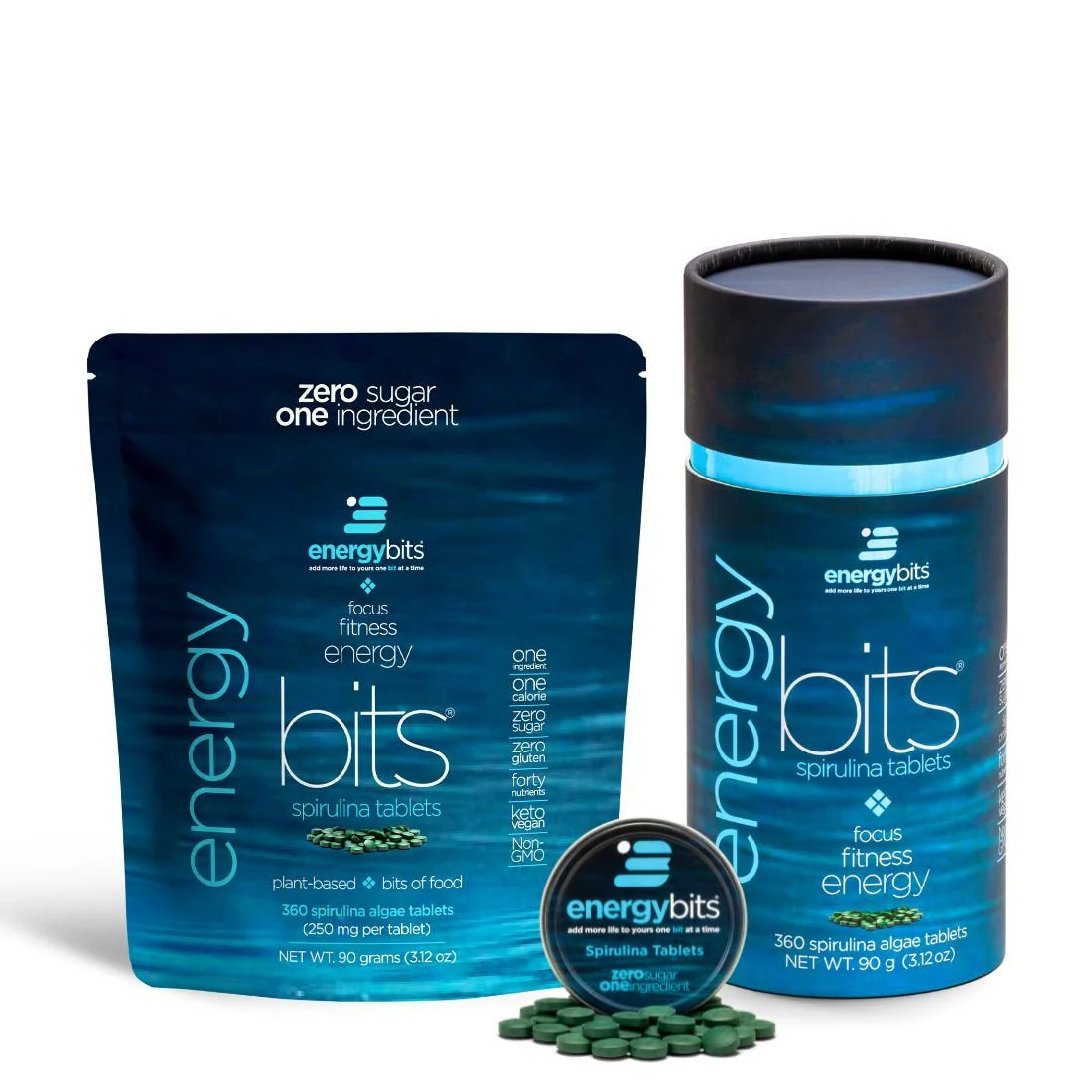 A small canister of ENERGYbits Spirulina next to its packaging, with several tablets visible in front. The canister and packaging are blue with product information and branding.