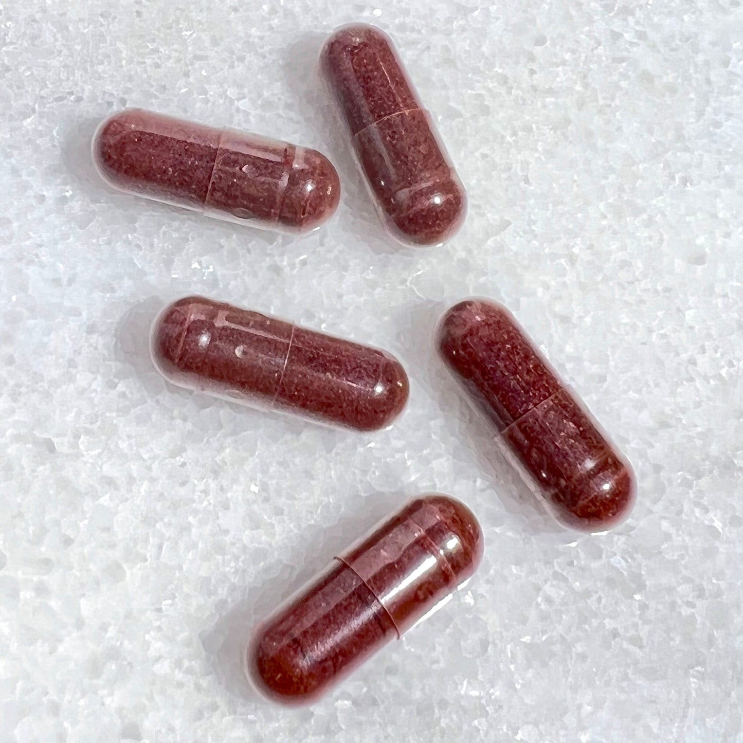 Five red capsules on a white textured surface