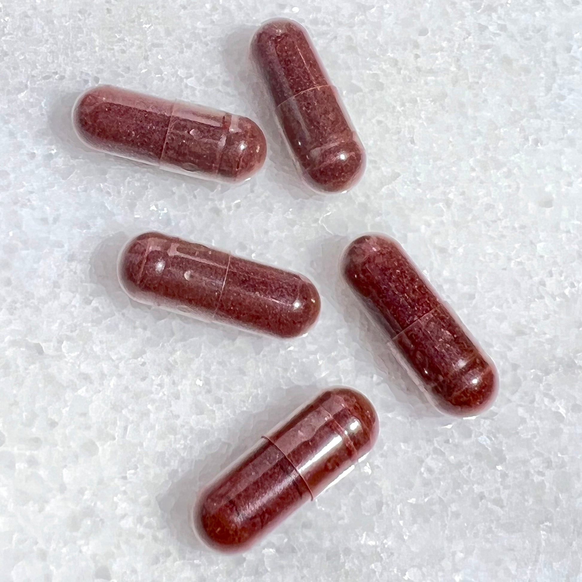 Five red capsules on a white textured surface