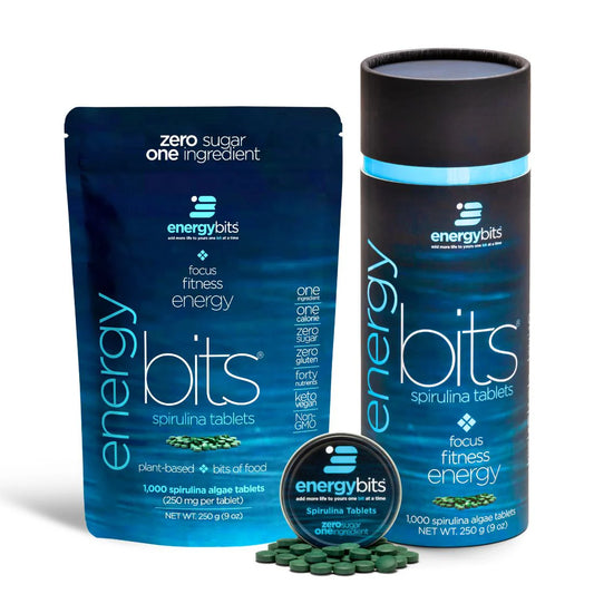 A canister and a pouch of ENERGYbits Spirulina tablets, with the product's benefits highlighted. The canister is black with blue accents, and the pouch is blue with text detailing the product's use for energy and fitness.