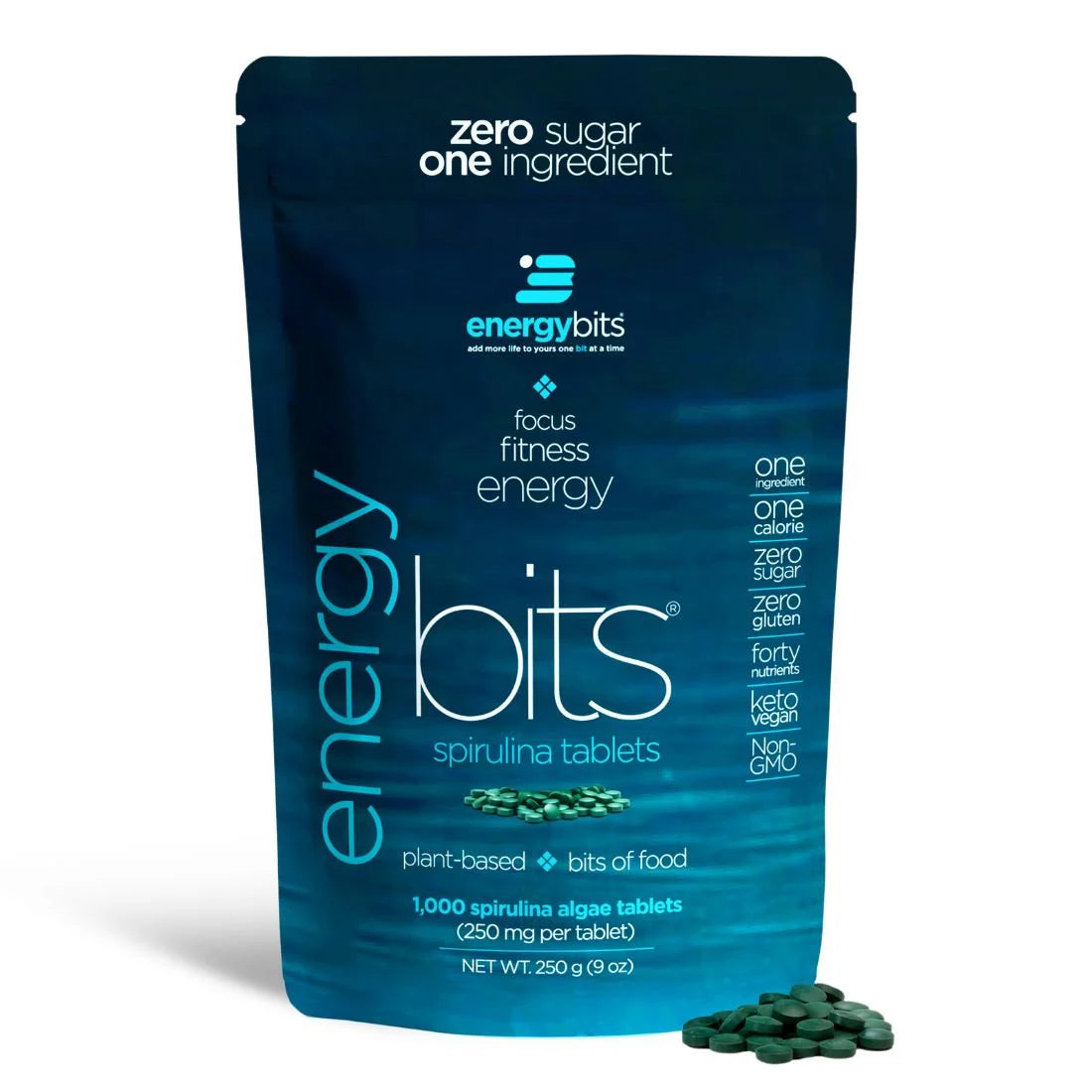 A large blue bag of ENERGYbits Spirulina plant-based tablets, with the product's benefits listed and a single spirulina tablet displayed in front.
